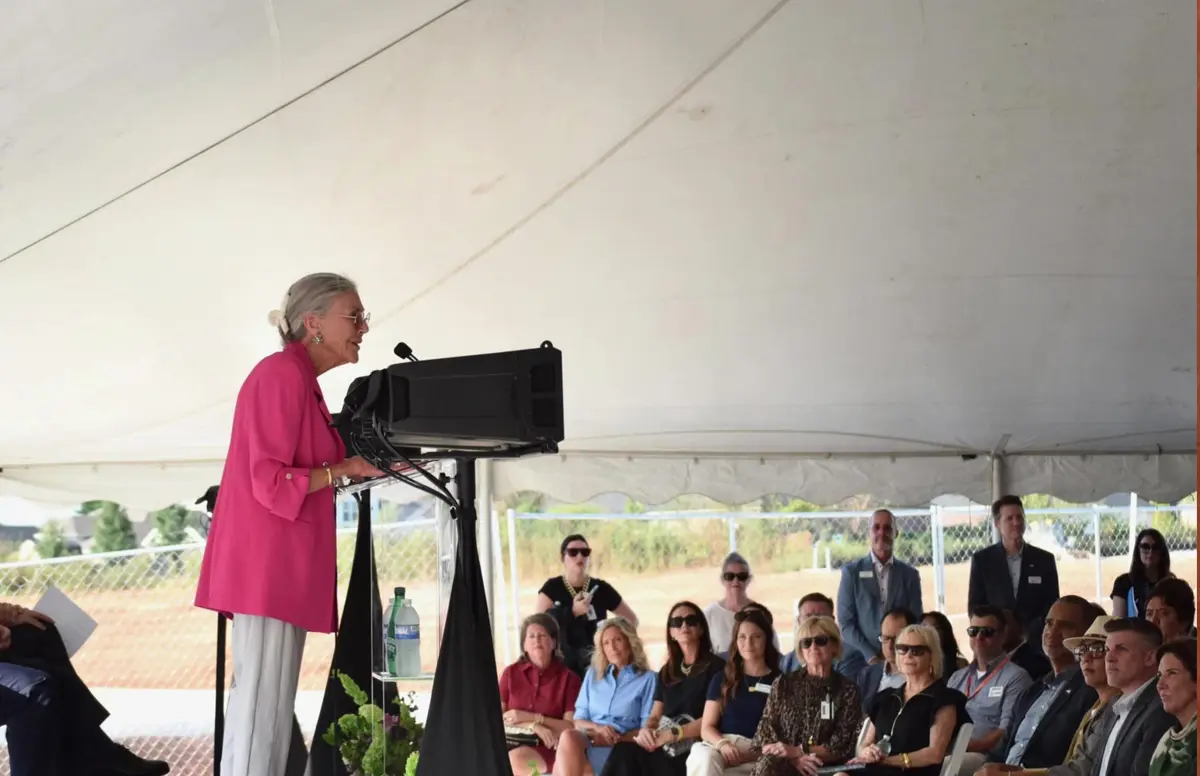 Groundbreaking ceremony for the AWSOM Whole Health Campus in Bentonville, Arkansas, with a speaker at a podium under a white event tent and guests seated on the cleared construction site