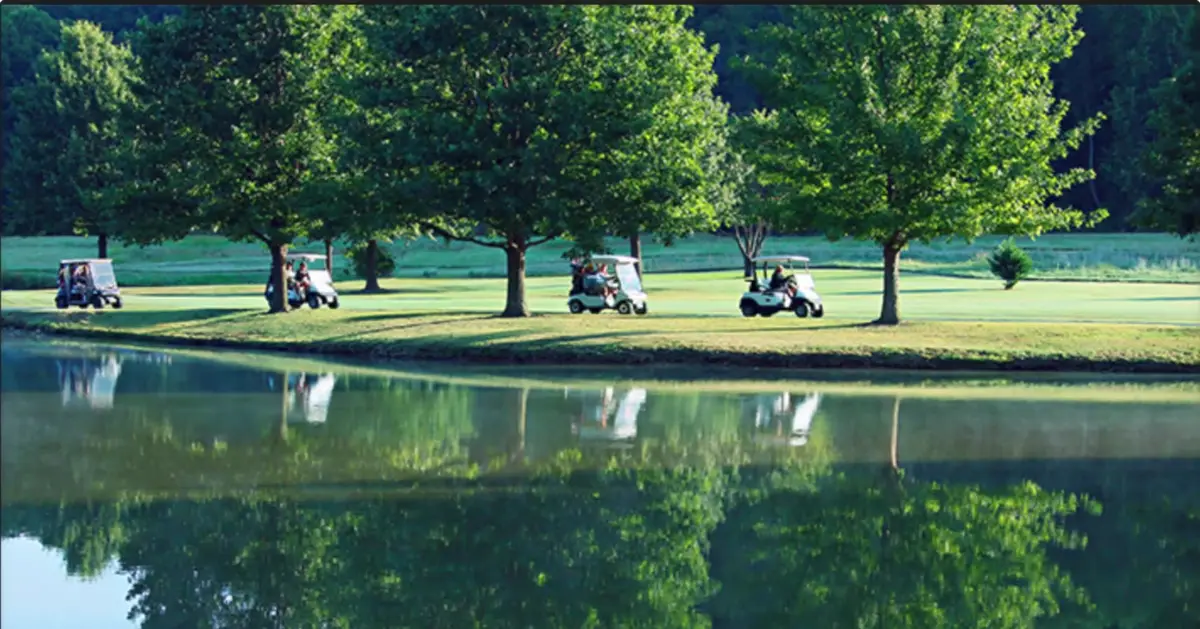 Golf carts on a tree-lined fairway reflected in a still lake at a Bella Vista, Arkansas golf course