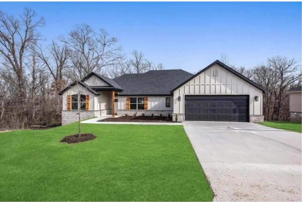 Newly built white modern farmhouse with a black garage door on a wooded lot in Bella Vista, Arkansas