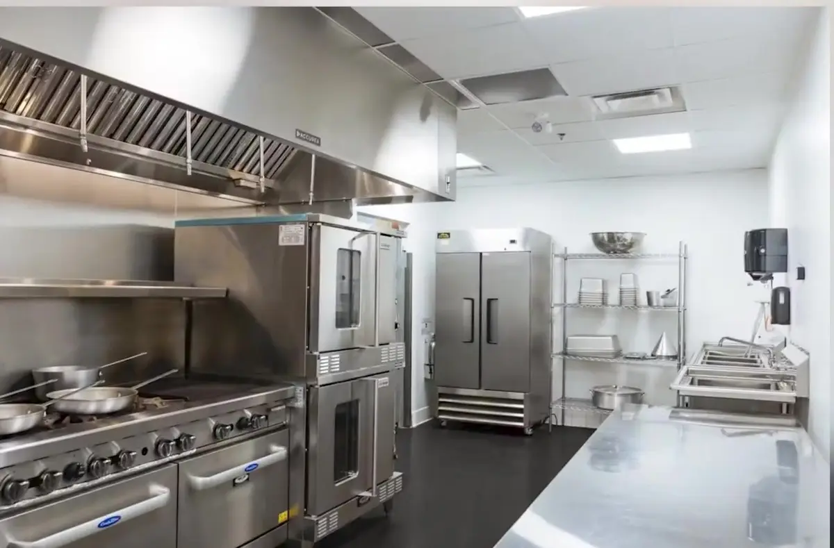 Empty stainless steel commercial kitchen with ranges, convection ovens and prep counters