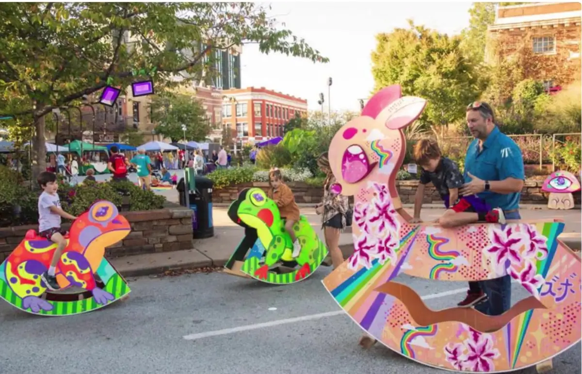 Children playing on brightly painted animal rocking sculptures at a downtown street festival in Northwest Arkansas