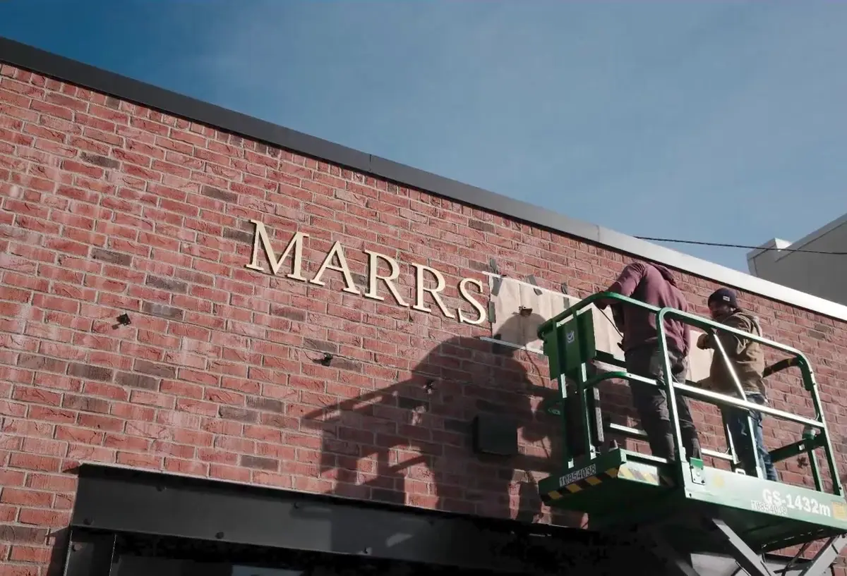 Workers on a lift installing brass lettering on the brick facade of a new Main Street shop in Bentonville, Arkansas