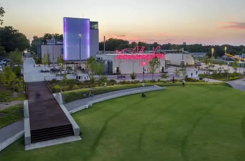 Aerial view of the Momentary in Bentonville at sunset, with its green lawn, lit tower and neon sign