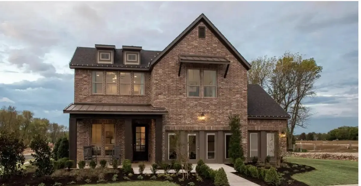 Two-story brick new construction home with a covered front porch in a Northwest Arkansas subdivision at dusk