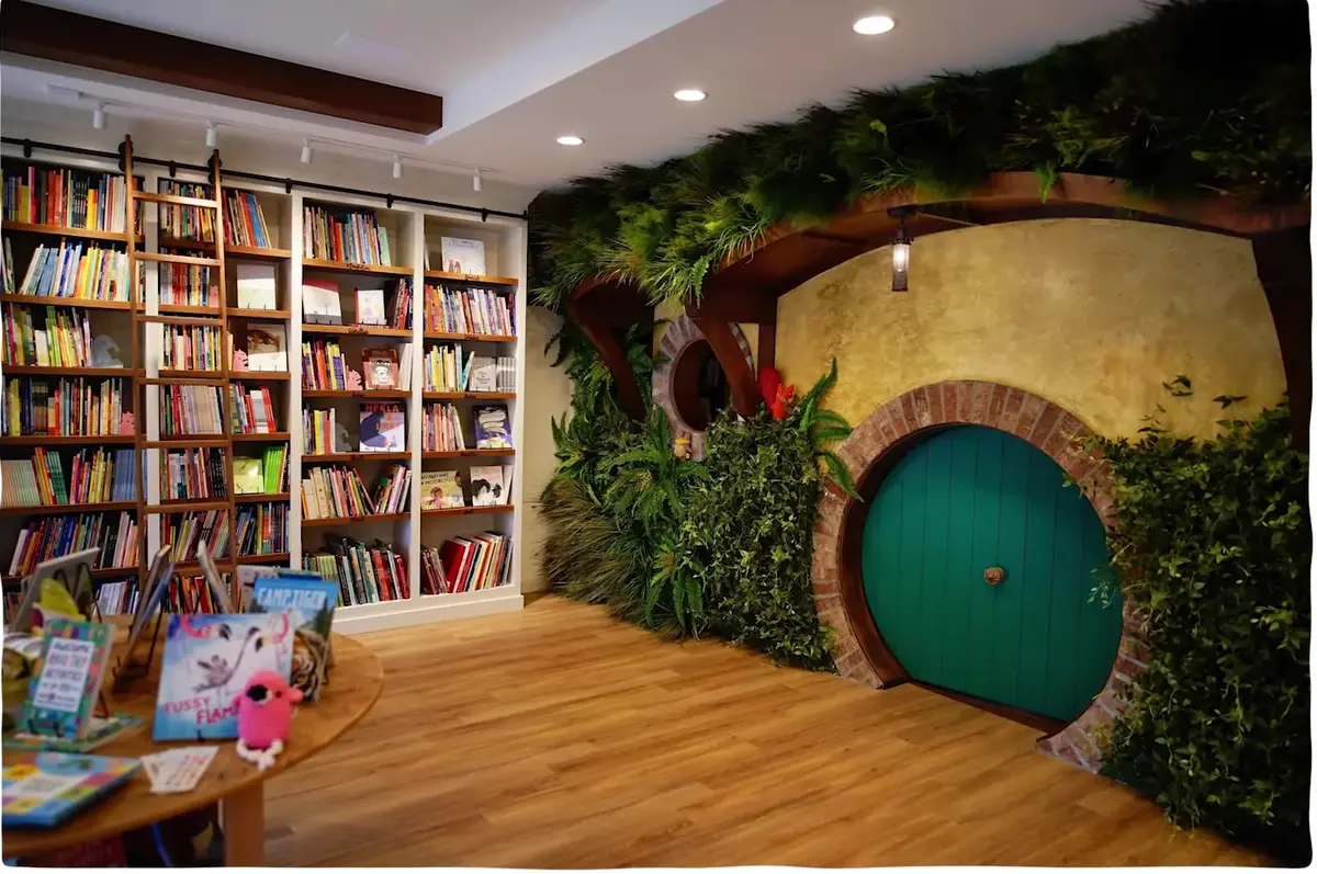 Children's bookstore interior with a round green hobbit-style door set into a planted wall in Northwest Arkansas