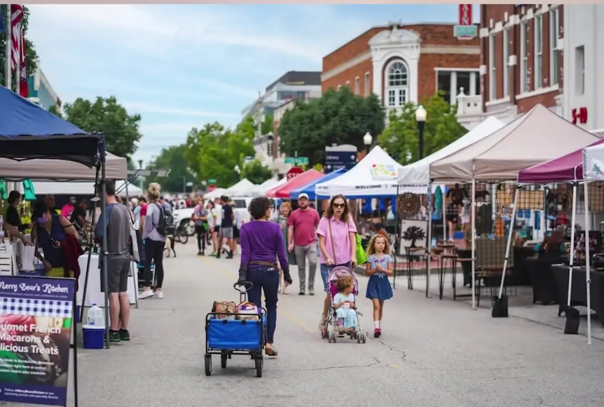 Shoppers walking among vendor tents at a busy downtown farmers market in Northwest Arkansas