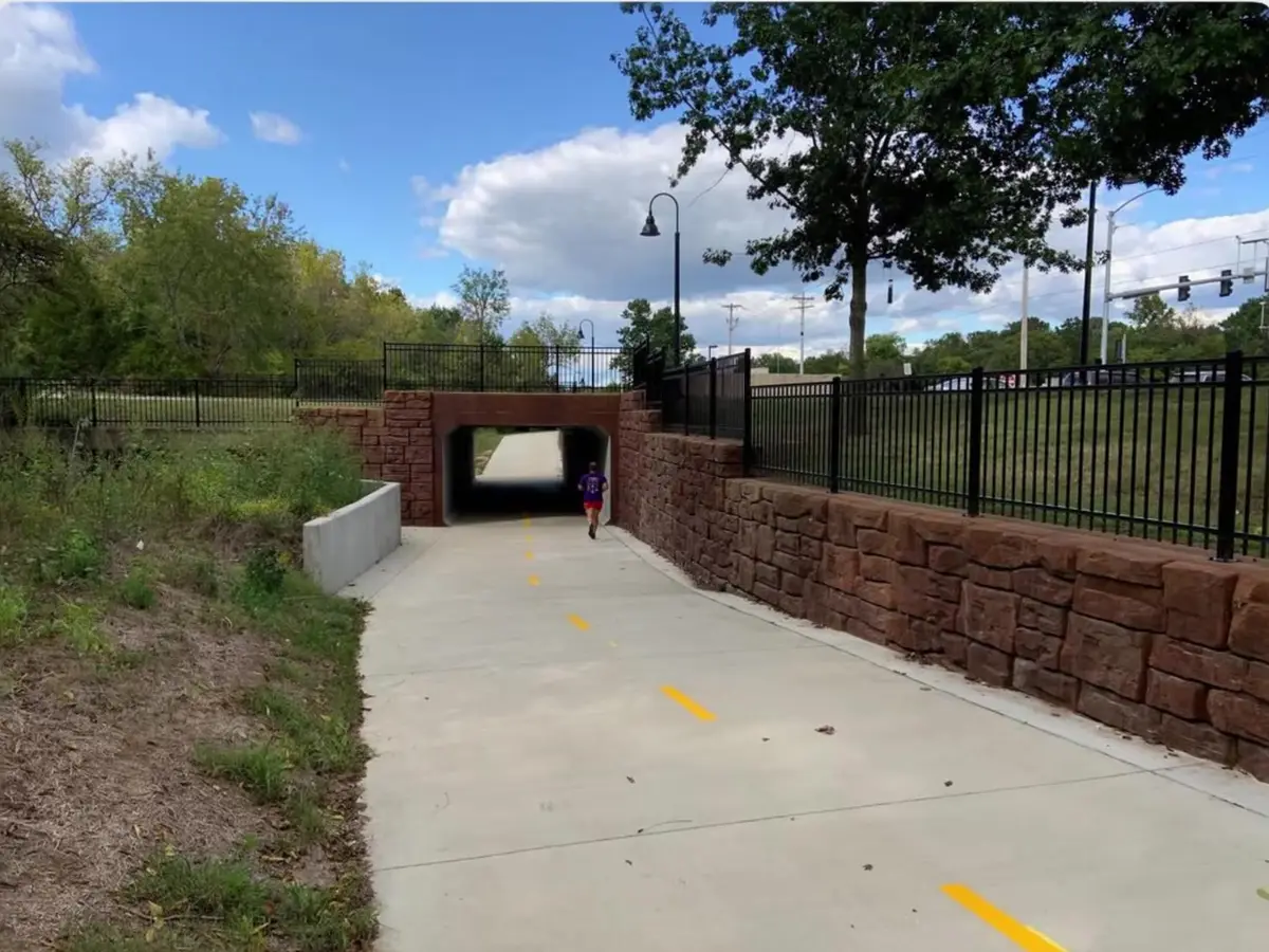 Runner entering a stone-walled underpass on a newly built paved greenway trail in Northwest Arkansas