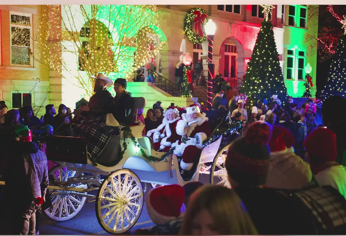 Santa and Mrs. Claus ride a horse-drawn carriage past a courthouse square covered in Christmas lights in Northwest Arkansas