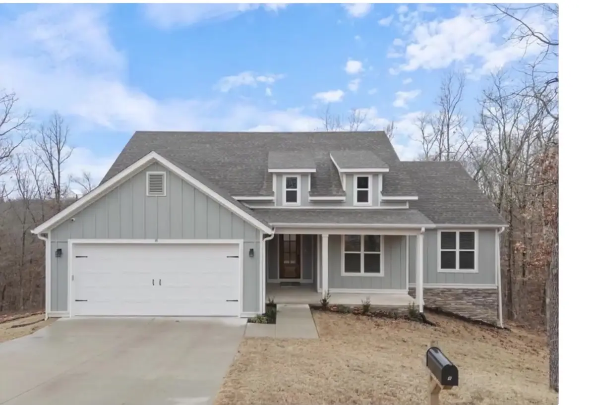 Newly built gray board-and-batten home with dormer windows on a wooded Northwest Arkansas hillside lot