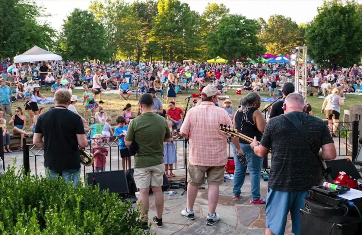 Band performing to a large lawn crowd at a free outdoor summer concert in a Northwest Arkansas park