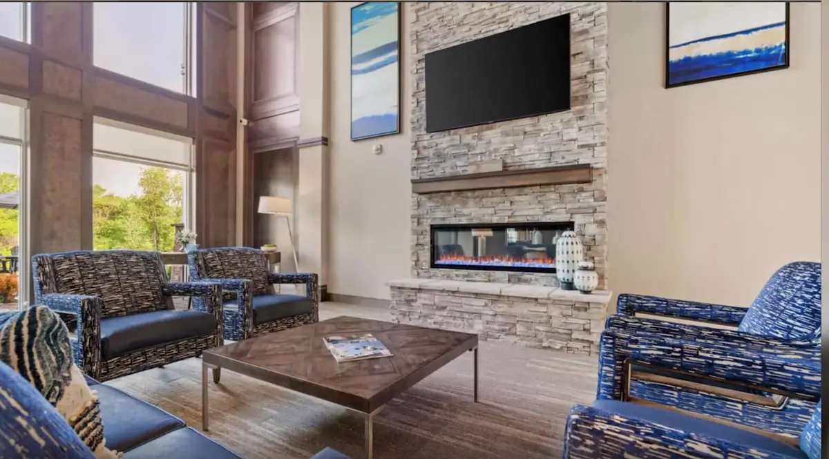 Common-area lounge with a stone fireplace, armchairs and tall windows in a Northwest Arkansas residential community