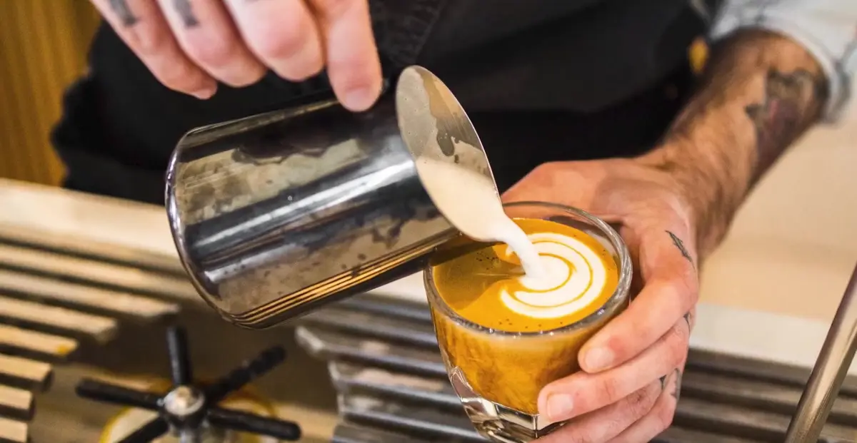 Barista pouring steamed milk into an espresso drink at a Northwest Arkansas specialty coffee bar
