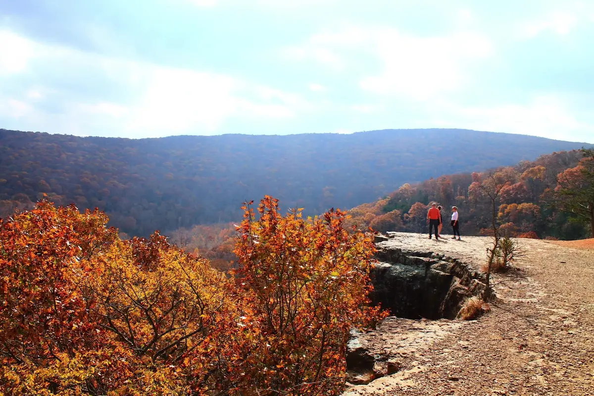 Hikers standing on a sandstone bluff overlooking an Ozark valley in peak fall color in Northwest Arkansas