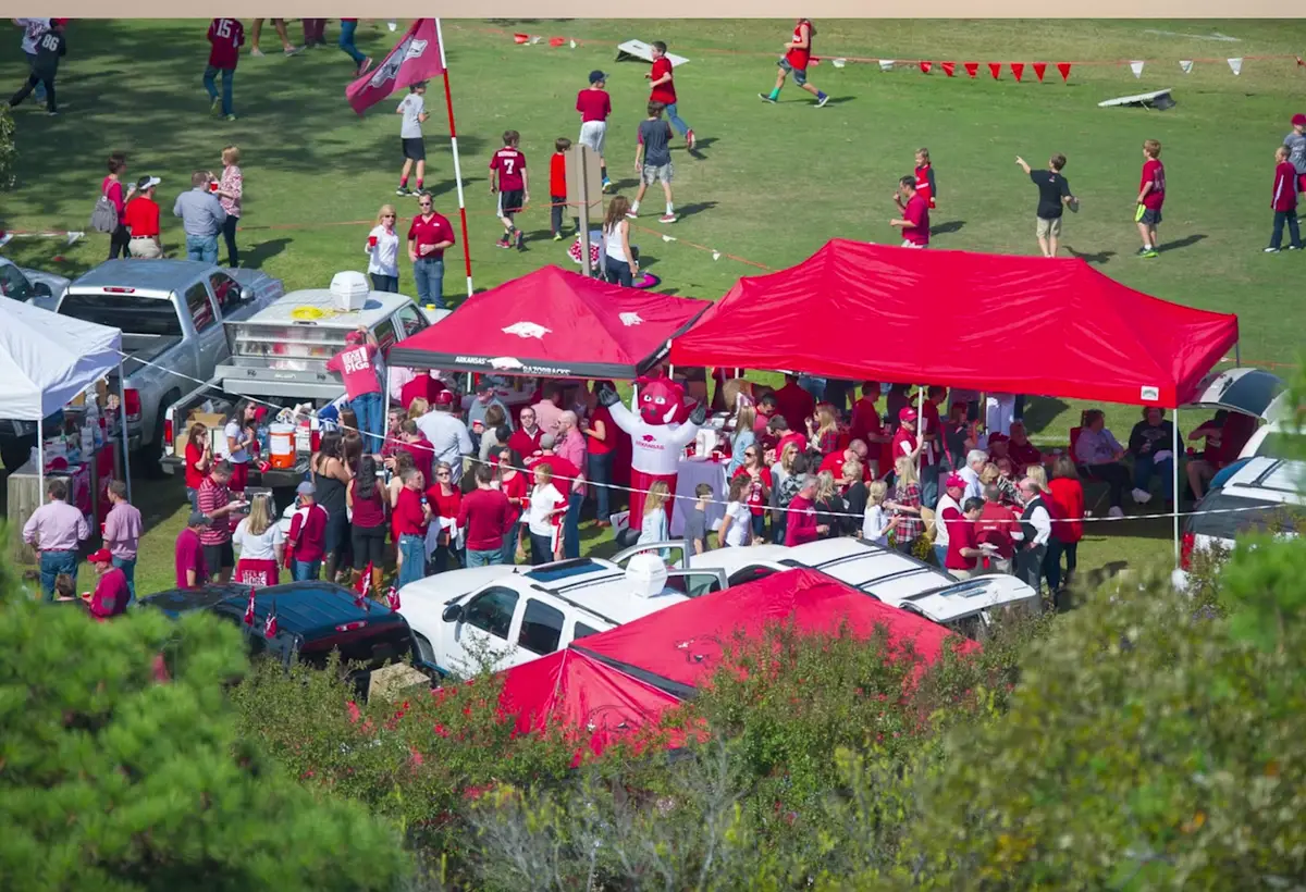 Razorback fans in red tailgating under canopies before a home football game in Fayetteville, Arkansas