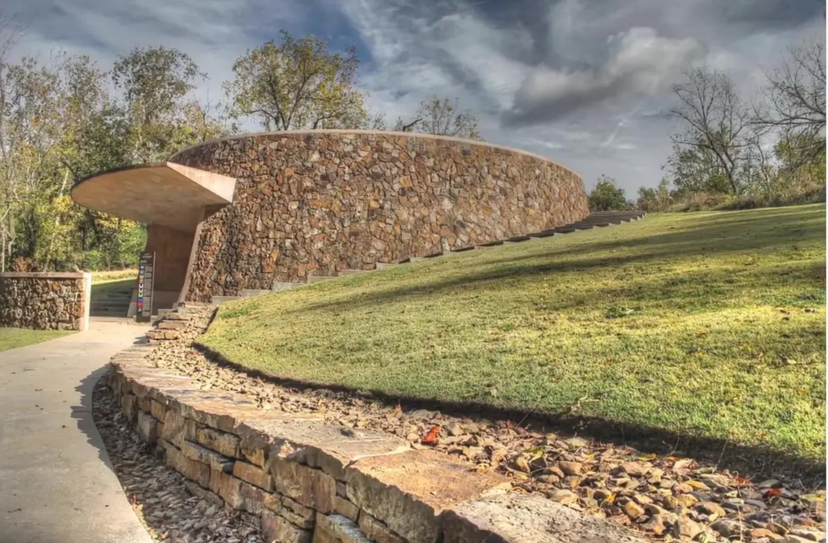 Circular stone skyspace structure with a concrete canopy set into a hillside on the Crystal Bridges art trail in Bentonville
