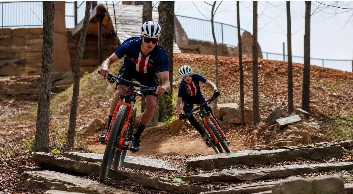 Two USA Cycling national team riders in USA jerseys riding down a rock-slab mountain bike trail through the woods in Bentonville, Arkansas