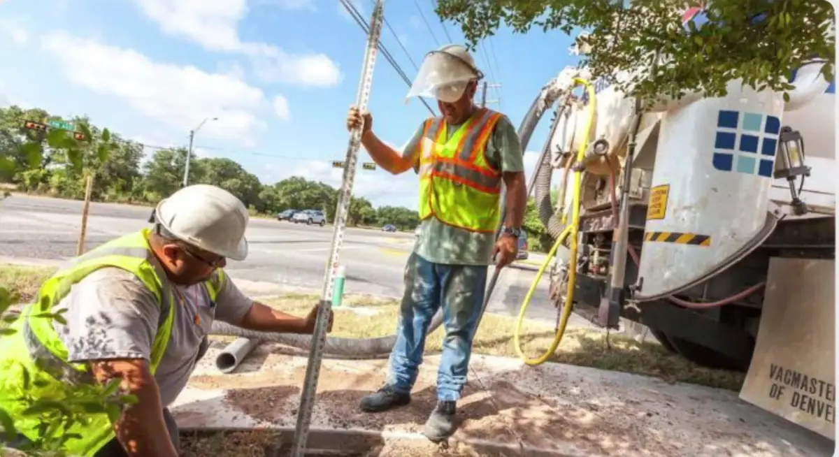 Utility crew in hard hats and high-visibility vests installing roadside infrastructure at a Northwest Arkansas subdivision