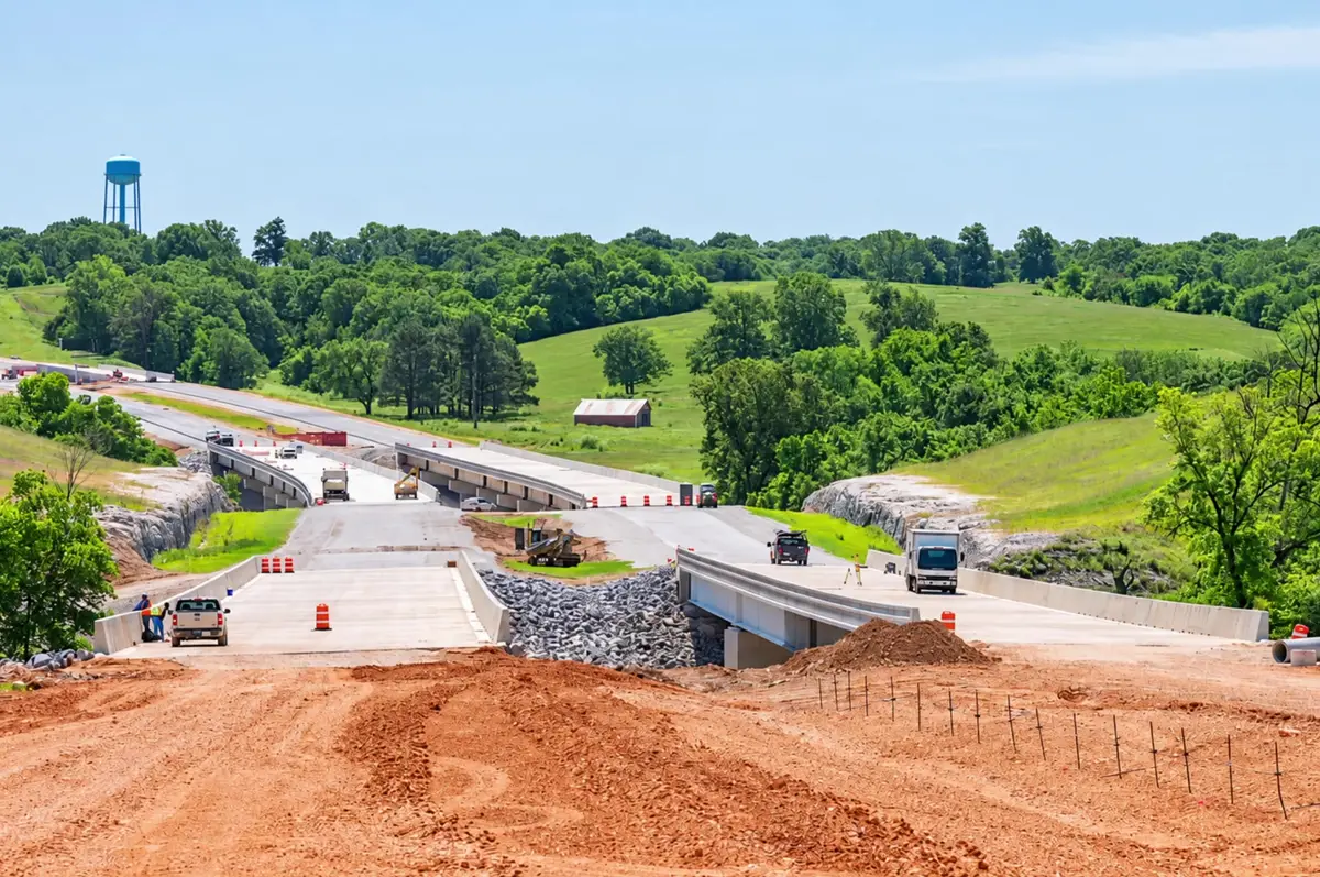 New four-lane highway under construction through green Northwest Arkansas hills, part of the road work connecting XNA to Interstate 49