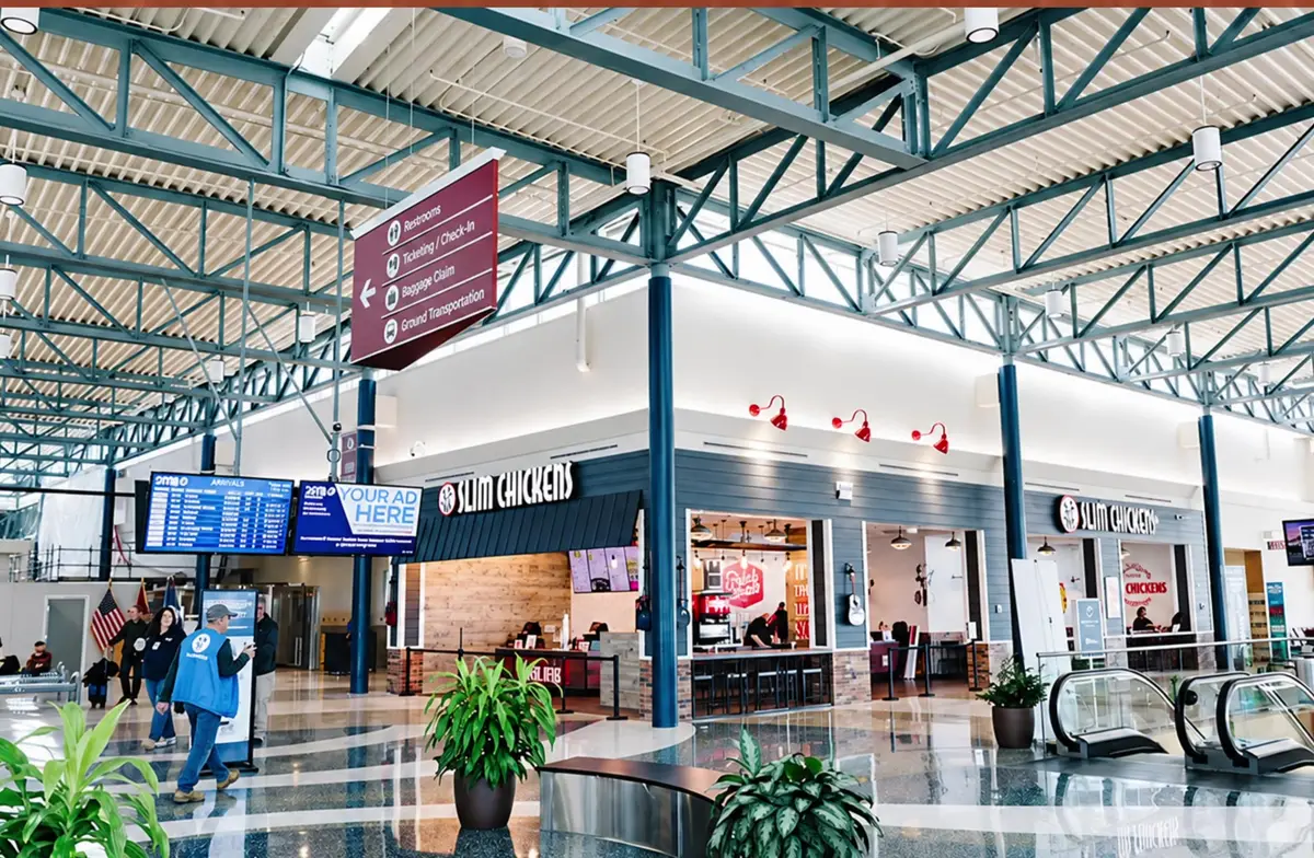 Concourse interior at Northwest Arkansas National Airport (XNA), with flight information screens, restaurants and escalators